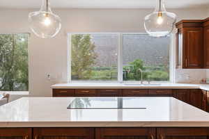 Kitchen featuring black electric cooktop, light stone countertops, sink, and pendant lighting