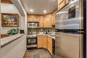 Kitchen with backsplash, light stone counters, light brown cabinets, and stainless steel appliances