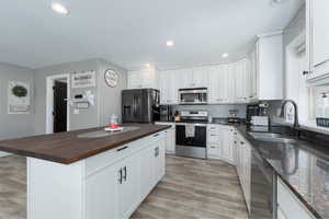 Kitchen featuring stainless steel appliances, sink, a center island, white cabinetry, and butcher block counters