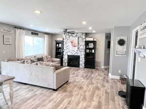 Living room with a stone fireplace, ceiling fan, and light hardwood / wood-style flooring