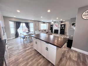 Kitchen with hardwood / wood-style floors, wood counters, a center island, a stone fireplace, and white cabinetry