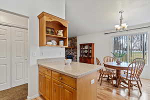 Kitchen with pendant lighting, an inviting chandelier, light wood-type flooring, light stone counters, and kitchen peninsula