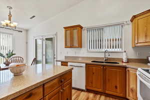 Kitchen with pendant lighting, lofted ceiling, white appliances, sink, and a chandelier