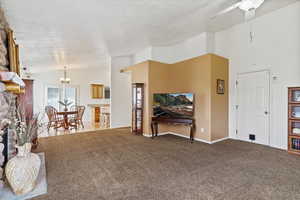 Living room with carpet floors, a fireplace, ceiling fan with notable chandelier, and lofted ceiling