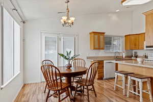 Dining space with light hardwood / wood-style flooring, vaulted ceiling, sink, and an inviting chandelier