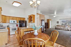 Dining area with sink, high vaulted ceiling, ceiling fan with notable chandelier, and light hardwood / wood-style flooring