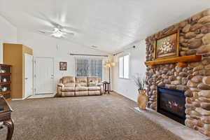 Carpeted living room with ceiling fan, a stone fireplace, lofted ceiling, and a textured ceiling