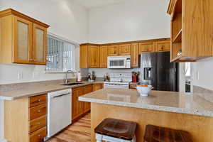 Kitchen featuring light stone countertops, a towering ceiling, a breakfast bar, white appliances, and sink