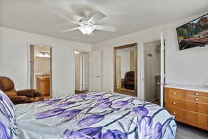 Carpeted bedroom featuring ensuite bathroom, a closet, and ceiling fan