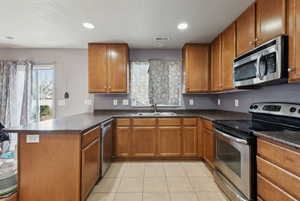 Kitchen featuring light tile patterned floors, kitchen peninsula, sink, and appliances with stainless steel finishes