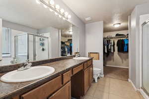 Bathroom featuring tile patterned floors, vanity, a shower with shower door, and a textured ceiling