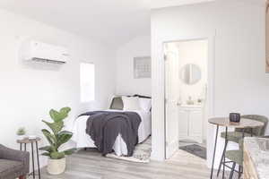 Bedroom featuring connected bathroom, sink, a wall unit AC, light hardwood / wood-style floors, and lofted ceiling