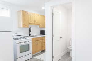 Kitchen with light brown cabinetry, sink, light hardwood / wood-style floors, and white appliances