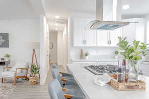 Kitchen with stainless steel gas stovetop, island range hood, white cabinetry, and light hardwood / wood-style flooring