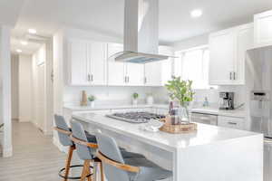 Kitchen with a kitchen bar, appliances with stainless steel finishes, island range hood, and white cabinetry