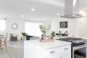 Kitchen with white cabinets, island range hood, light hardwood / wood-style floors, and stainless steel range with gas stovetop