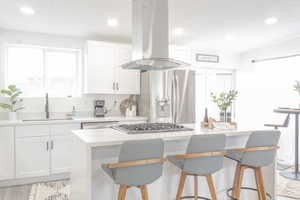 Kitchen with white cabinets, sink, a breakfast bar area, island range hood, and stainless steel appliances