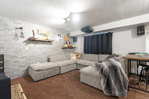 Living room featuring a textured ceiling, dark carpet, and brick wall