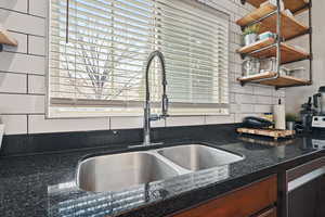 Kitchen with backsplash, dark stone countertops, and sink