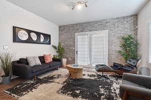 Living room with carpet flooring, a wealth of natural light, a textured ceiling, and brick wall