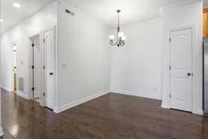 Empty room featuring dark hardwood / wood-style flooring, ornamental molding, and an inviting chandelier