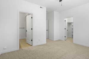 Unfurnished bedroom with a closet, light colored carpet, a spacious closet, and ceiling fan