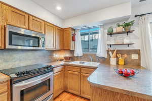 Kitchen with decorative backsplash, sink, light hardwood / wood-style flooring, and appliances with stainless steel finishes