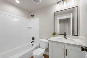 Bathroom with visible vents, toilet, wood finished floors, vanity, and washtub / shower combination