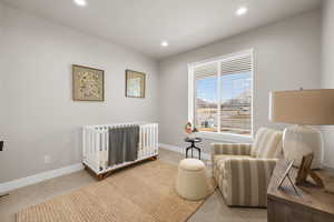 Bedroom with recessed lighting, light colored carpet, a nursery area, and baseboards