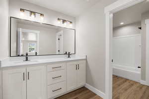 Full bathroom featuring double vanity, wood finished floors, a sink, and baseboards