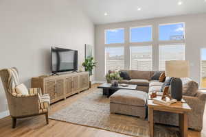 Living area featuring baseboards, high vaulted ceiling, wood finished floors, and recessed lighting