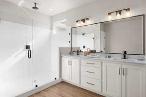 Bathroom with a stall shower, double vanity, a sink, and wood finished floors