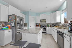 Kitchen with a center island, stainless steel appliances, tasteful backsplash, white cabinetry, and sink