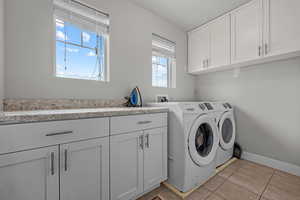 Washroom featuring washer and dryer, cabinets, and light tile patterned flooring