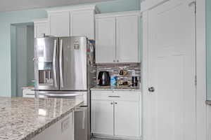 Kitchen featuring white cabinets, tasteful backsplash, light stone counters, and stainless steel fridge