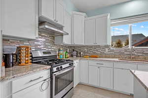 Kitchen featuring range hood, backsplash, white cabinets, stainless steel range with gas stovetop, and sink