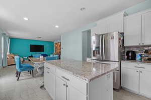 Kitchen with white cabinets, a center island, decorative backsplash, and stainless steel refrigerator with ice dispenser