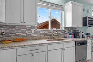 Kitchen with stainless steel appliances, sink, white cabinets, light stone counters, and decorative backsplash