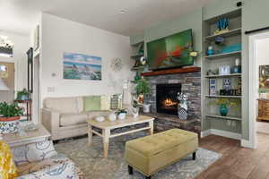 Living room with a notable chandelier, a stone fireplace, and wood-type flooring