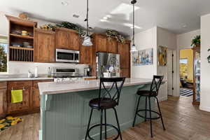 Kitchen with stainless steel appliances, pendant lighting, hardwood / wood-style floors, a center island, and a breakfast bar area