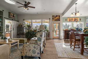 Living room with ceiling fan with notable chandelier, a textured ceiling, a barn door, and light hardwood / wood-style floors