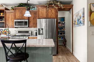 Kitchen with decorative light fixtures, light wood-type flooring, and appliances with stainless steel finishes