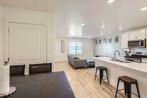 Kitchen featuring appliances with stainless steel finishes, light wood-type flooring, sink, white cabinets, and a breakfast bar area