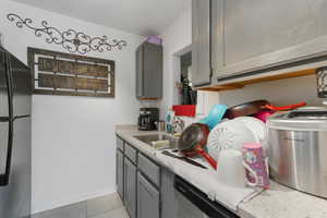 Kitchen featuring gray cabinetry, black refrigerator, sink, stainless steel dishwasher, and light tile patterned flooring