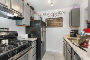 Kitchen with black refrigerator, gas stove, extractor fan, light tile patterned floors, and gray cabinets