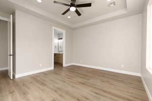 Unfurnished bedroom featuring ceiling fan, light hardwood / wood-style floors, a raised ceiling, and ensuite bath