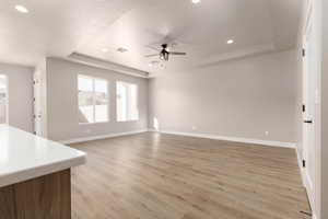 Unfurnished living room featuring a textured ceiling, a tray ceiling, ceiling fan, and light hardwood / wood-style floors