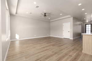 Unfurnished living room with light wood-type flooring, a raised ceiling, and ceiling fan