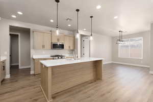 Kitchen with light brown cabinets, a kitchen island with sink, sink, decorative light fixtures, and range