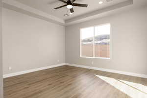 Spare room with a tray ceiling, ceiling fan, and hardwood / wood-style flooring